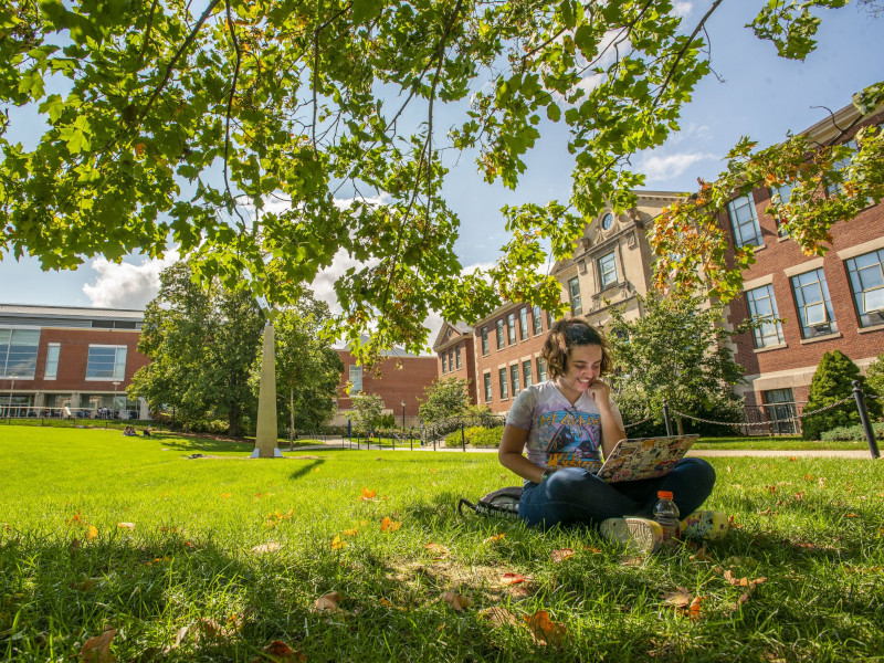 female student on her laptop sitting in front of castleman on grass